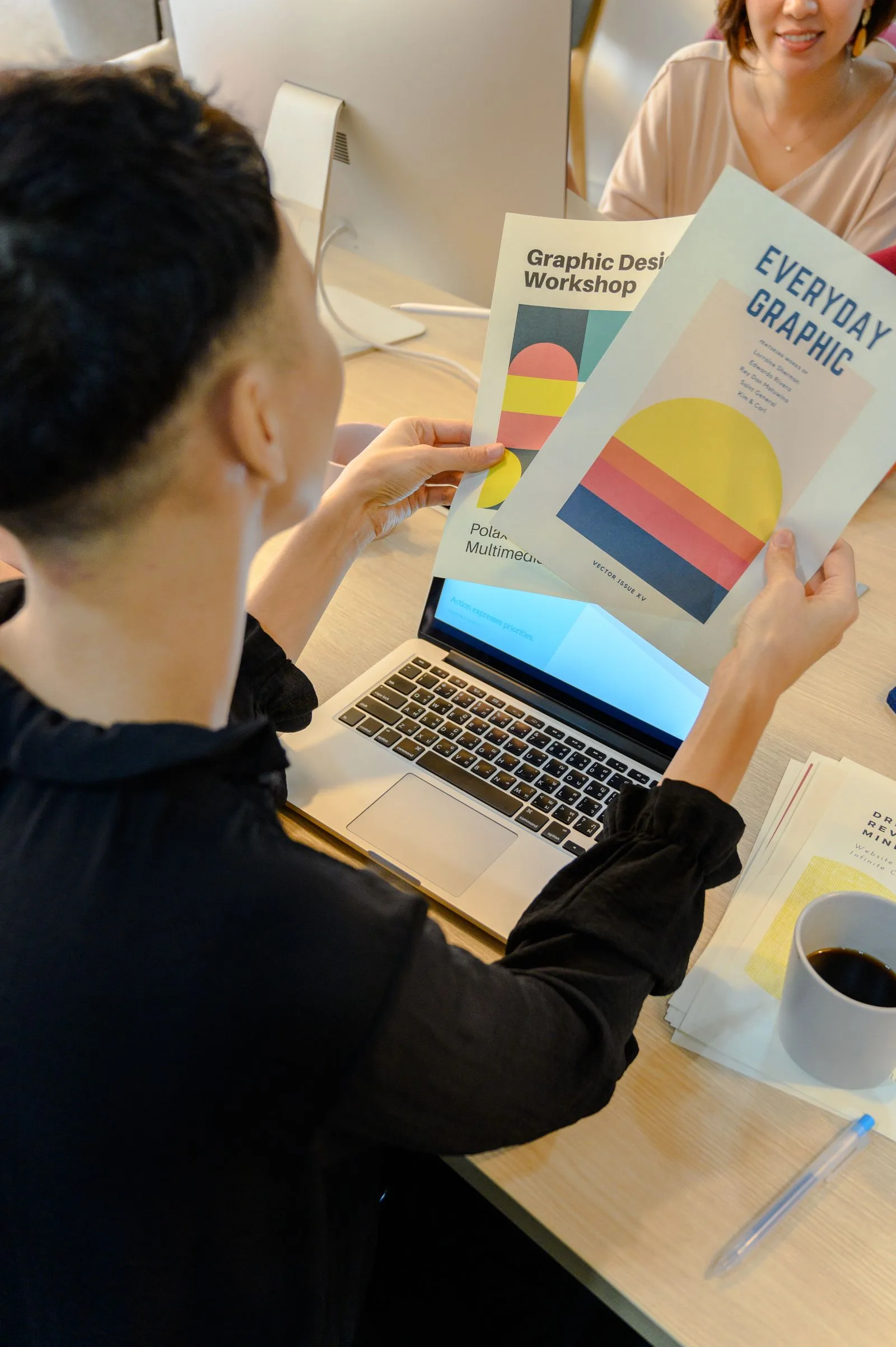 Professional reviewing colourful printed brochures beside a laptop, like checking AI-made Canva Craft designs before publishing